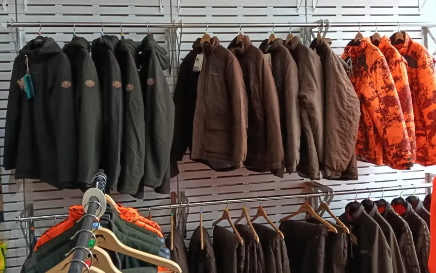 Jagdjacken in Grün, Braun und Signal-Orange an der Wand im Verkaufsraum
