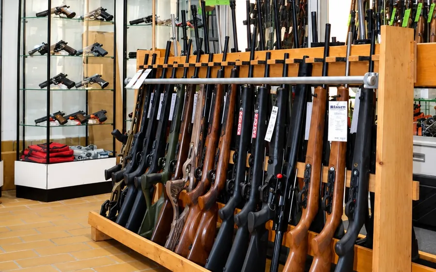 Büchsen mit Holz- und Kunststoffschaft im Holzständer im Verkaufsraum, dahinter Vitrinen mit Kurzwaffen