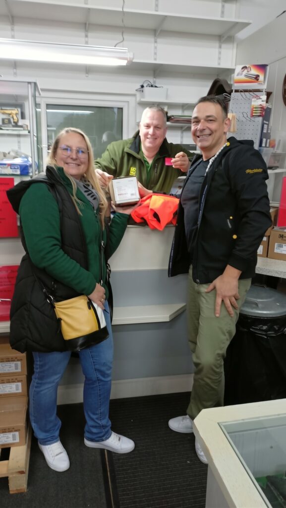 Stefan Geus hinter dem Ladentisch mit den Gewinnern des Tombola-Hauptpreises. Die Gewinnerin hält die Verpackung des Zielfernrohrs.